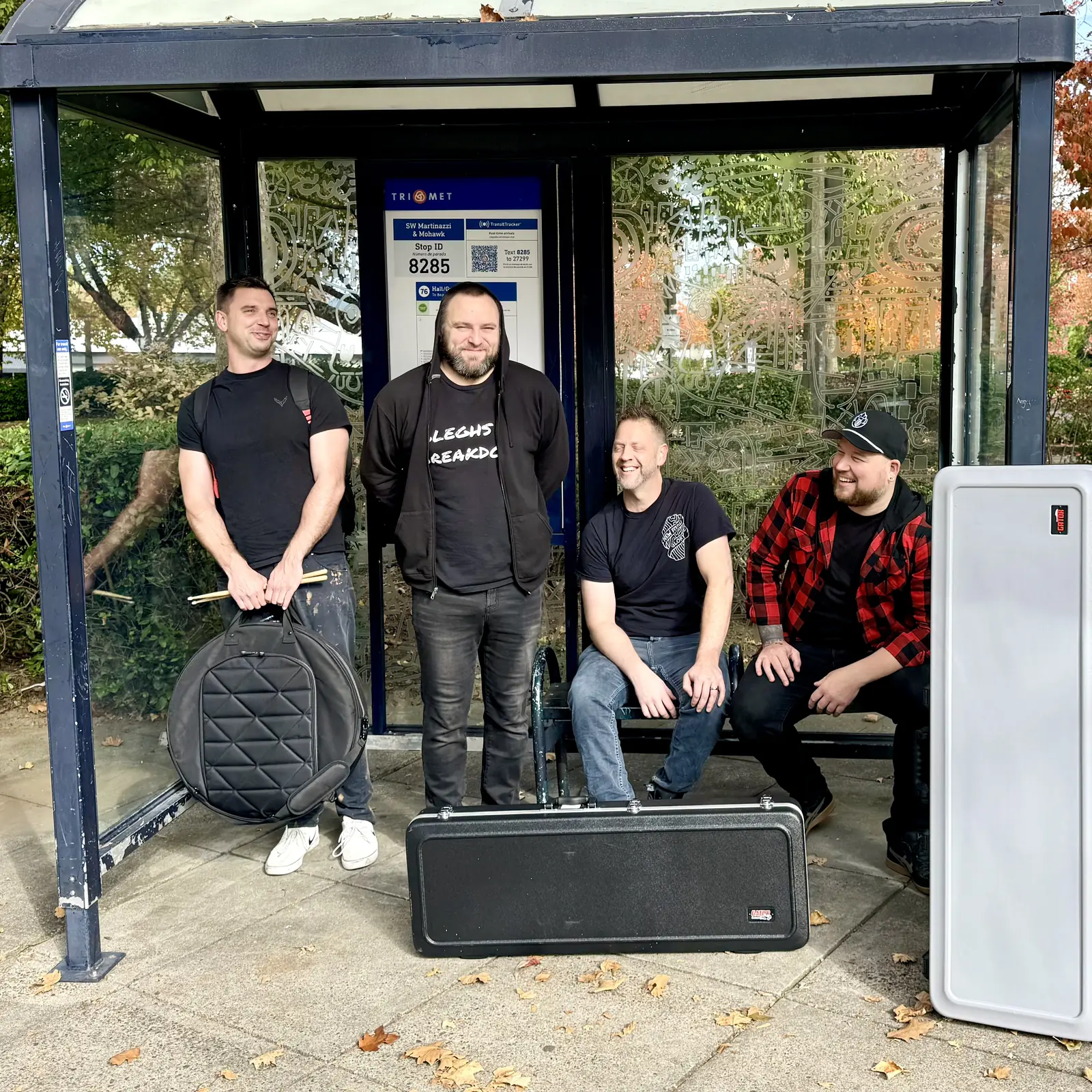 Kramer, Andrew, Michael and Graham of CARD3N at a TriMet bus stop with their drum, guitar and bass cases