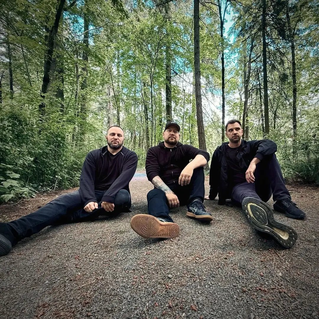 Graham, Andrew and Kramer sitting on a gravel trail in a tall green forest, all in black