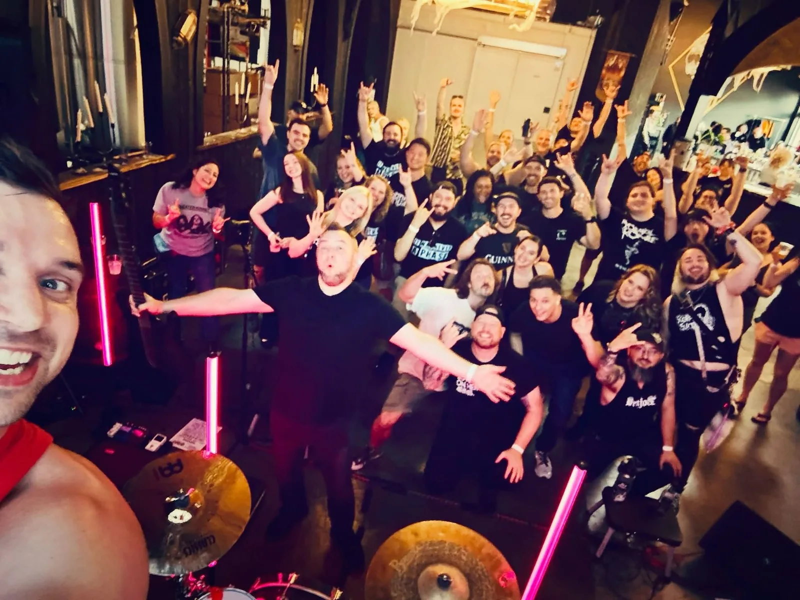 Selfie from behind the drum kit: a packed room of fans throwing horns and cheering at the stage