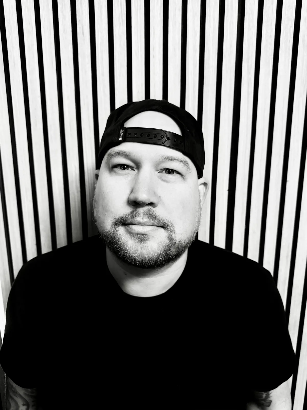 Graham in a backwards cap and black tee, in front of a slatted wall